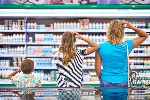 Eine Familie steht vor dem Kühlschrank in einem Supermarkt und kann sich nicht entscheiden, was sie kaufen möchte. 