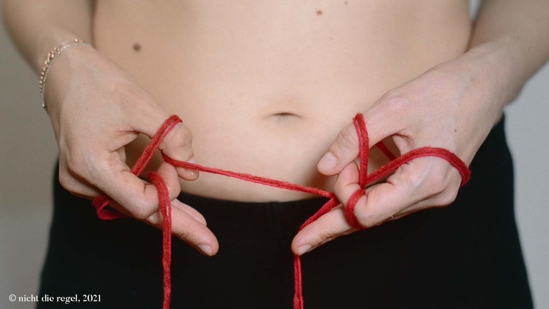 Eine Frau hält vor ihrem Bauch eine rote Schnur und wickelt diese um ihre Finger