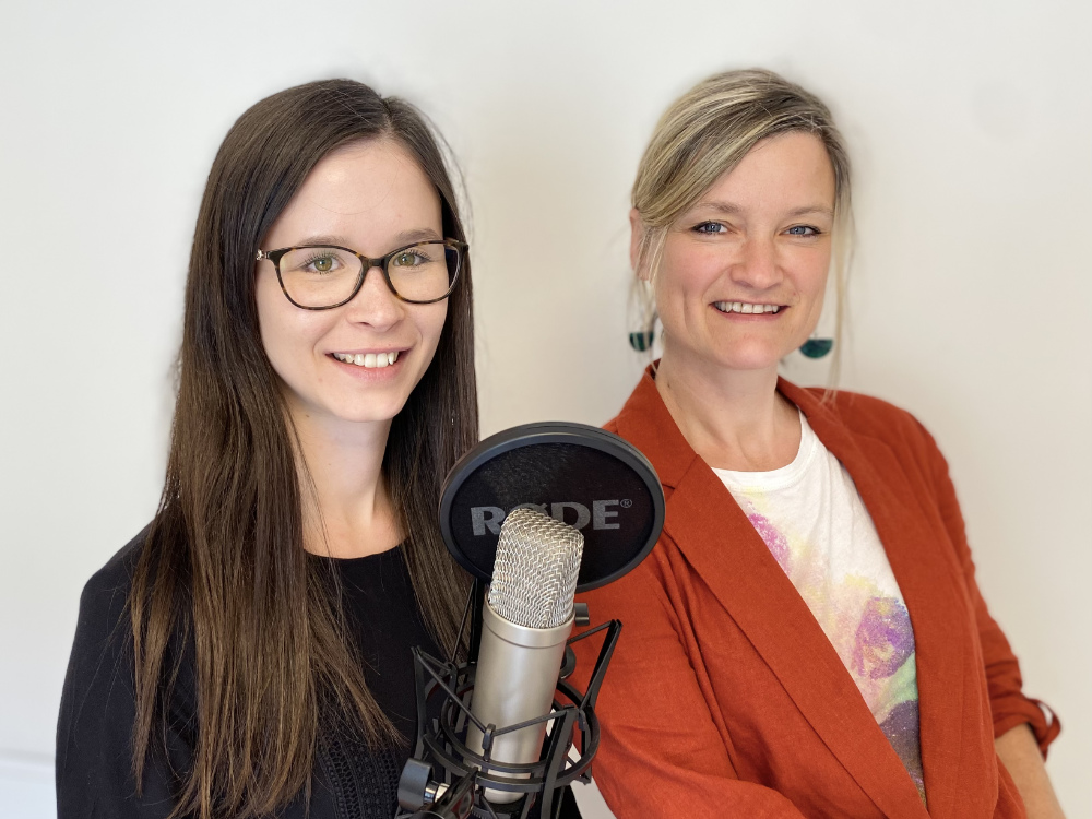 Zwei Frauen stehen nebeneinander und nehmen eine Podcast-Folge auf