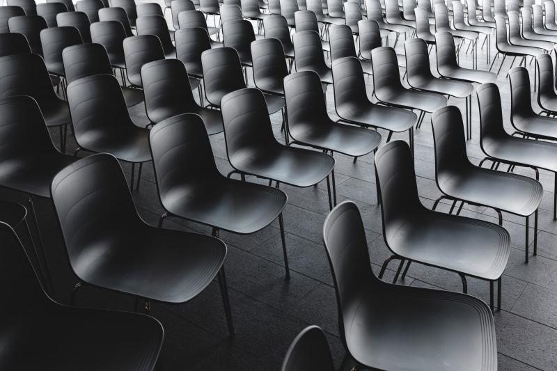 Es stehen ganz viele schwarze Stühle gereiht in einem Konferenzraum. 