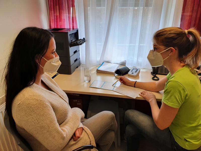 Zwei Frauen sitzen mit FP2-Masken in einem kleinen Besprechungszimmer. Die rechte Frau klärt ihre Patientin auf zum Thema Diabetes. 