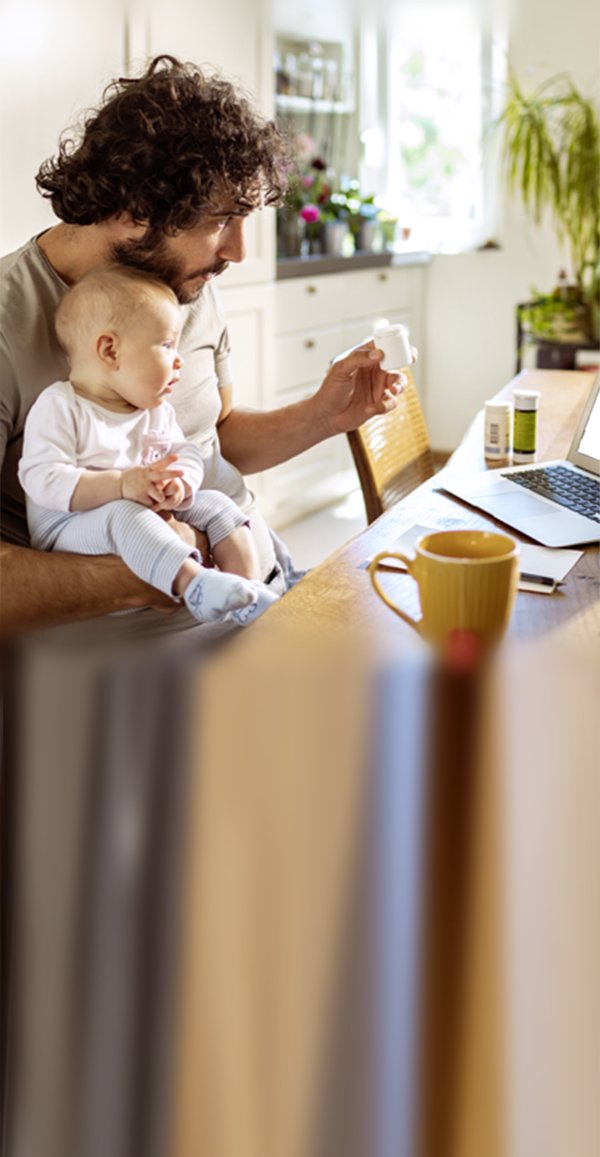 Mann mittleren Alters schaut sich die Website von „Gesund informiert“ an und hält dabei sein Baby auf dem Schoß