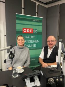 Ein Mann und eine Frau während einer Podcast-Aufnahme. Im Hintergrund ein Banner mit dem ORF Logo und der Aufschrift Radio, Fernsehen, Online.
