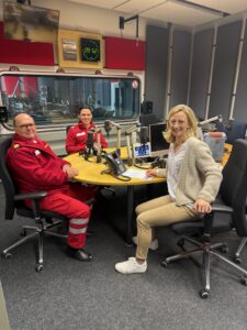 2 Männer in Rettungsanzügen und eine Moderatorin bei einer Podcast-Aufnahme