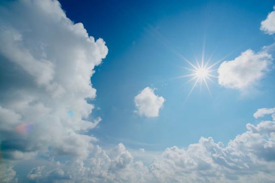 Hell strahlende Sonne auf blauem Wolkenhimmel.