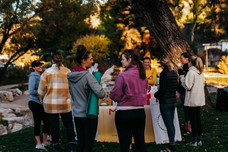 Gruppe von Frauen bei einem Outdoor-Wellness-Event mit Yoga-Matten und Infostand im Park